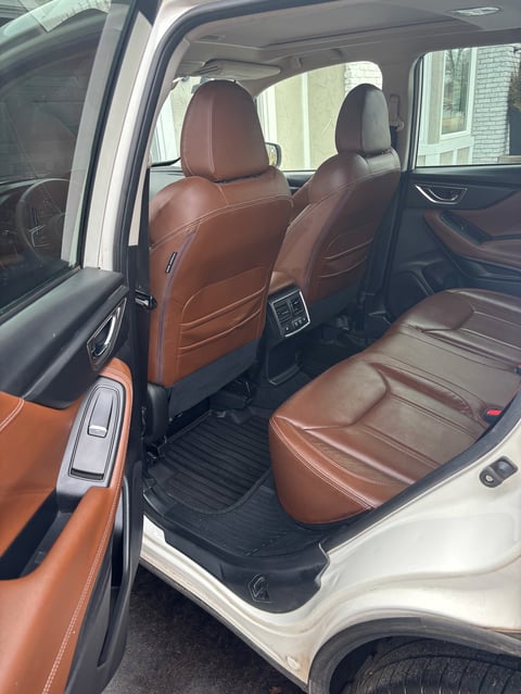 Interior view of a car with brown leather seats, showing front and rear seating with white door frame and black floor mat