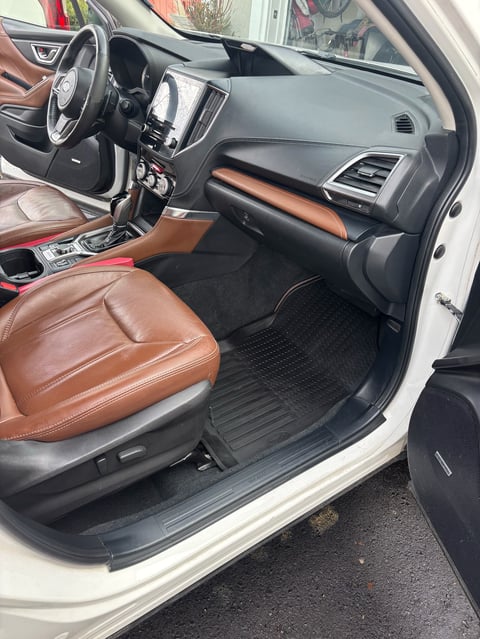 Interior of a modern car with brown leather driver seat, gray dashboard, touchscreen display, and steering wheel visible with door open