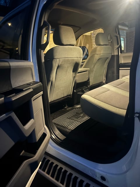 Interior of a pickup truck cabin at night showing gray upholstered front and rear seats with open driver side door