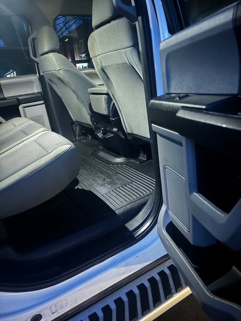 Interior of blue pickup truck showing cream-colored front seats, open door, black floor mat, and dashboard with mirrors visible