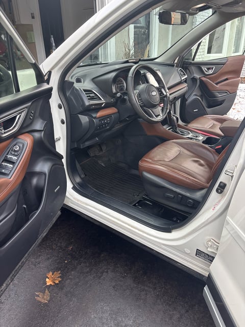 Interior view of white car with open driver door showing leather seats, steering wheel, and dashboard with brown and black accents